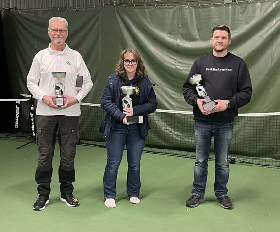 Three people are standing on a tennis court, each holding a price